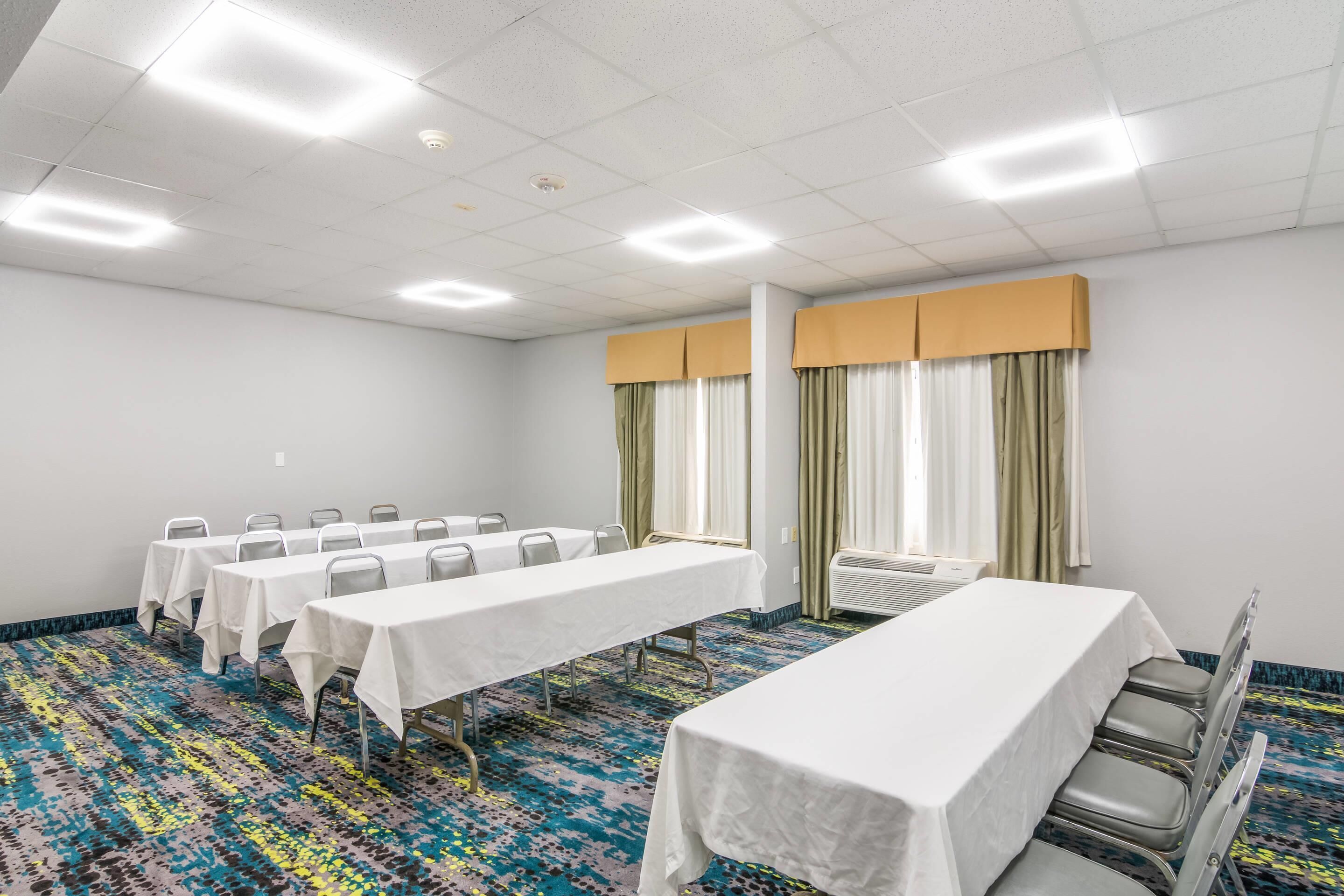 Une salle de conférence avec des tables et des chaises blanches, ainsi qu’un tapis à motifs.
