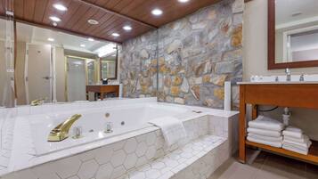A bathroom with a large bathtub, a wooden vanity, and a stone wall.
