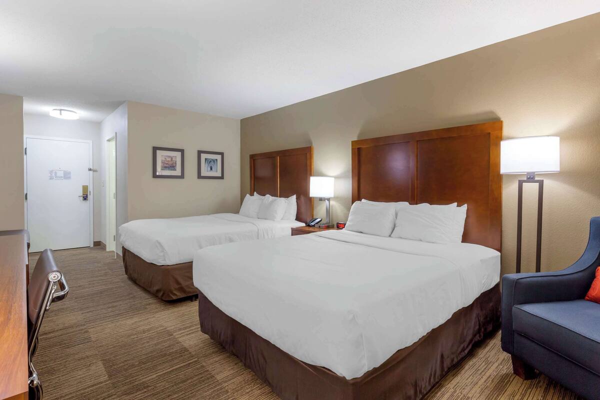 Una habitación de hotel con dos camas, un escritorio, una silla y una lámpara.