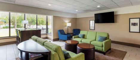 A modern hotel lobby with green sofas, a round table, and a flat-screen TV on the wall.