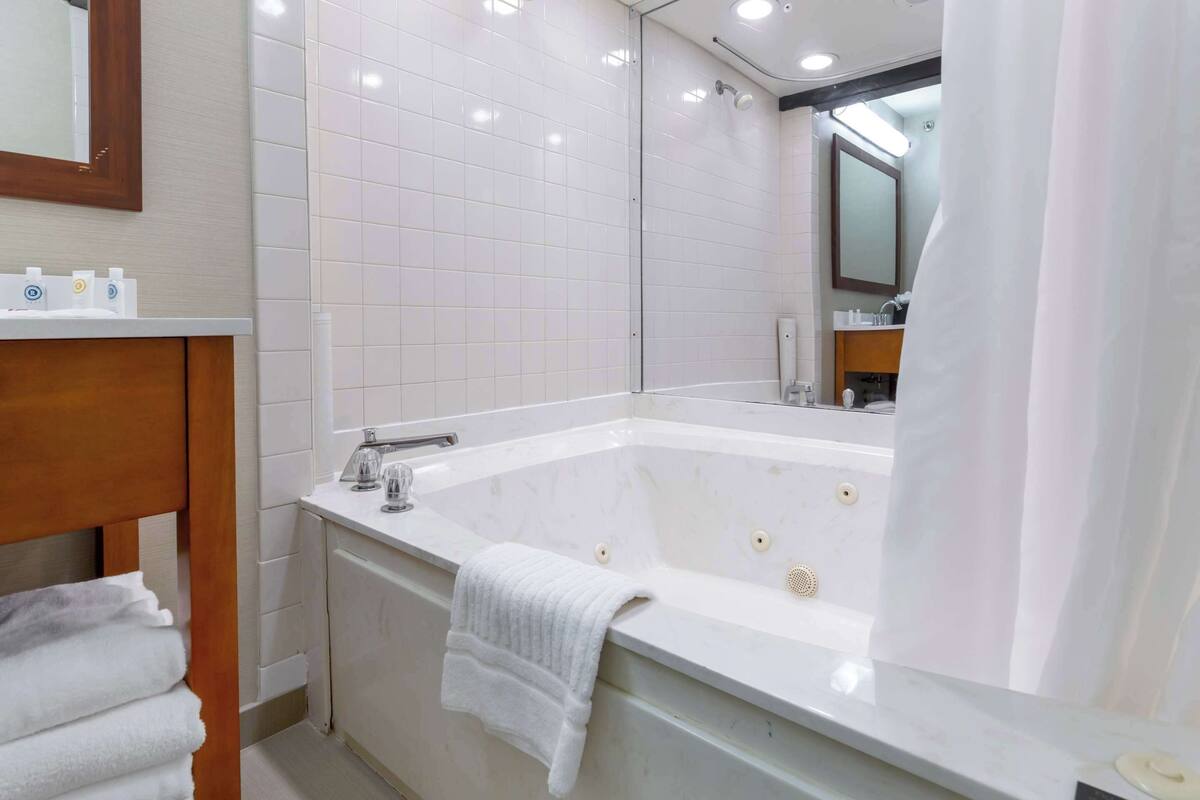 Un baño moderno con una bañera grande, un tocador de madera y un espejo sobre el lavabo.