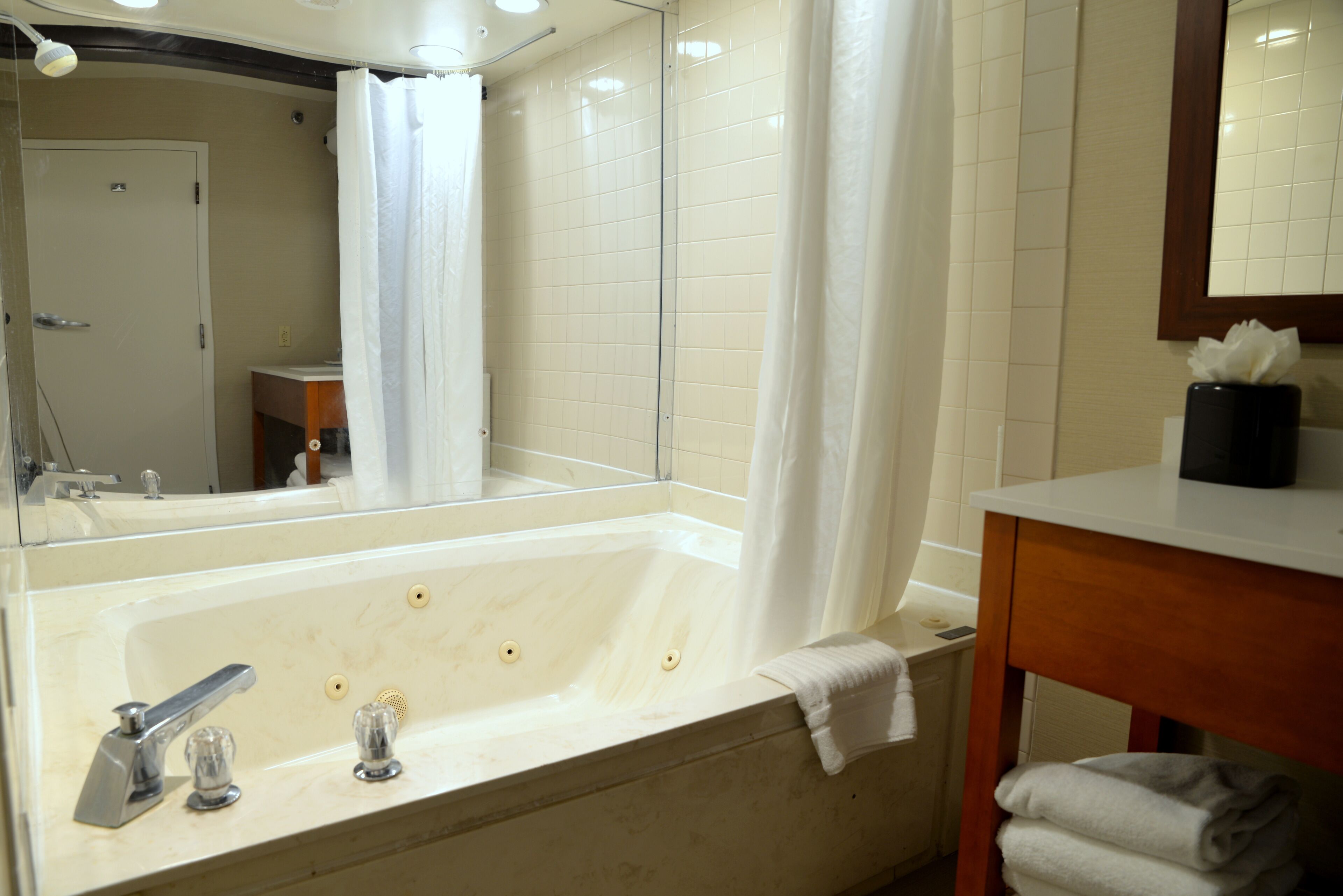 A bathroom with a large bathtub, a mirror, a sink, and a towel rack.