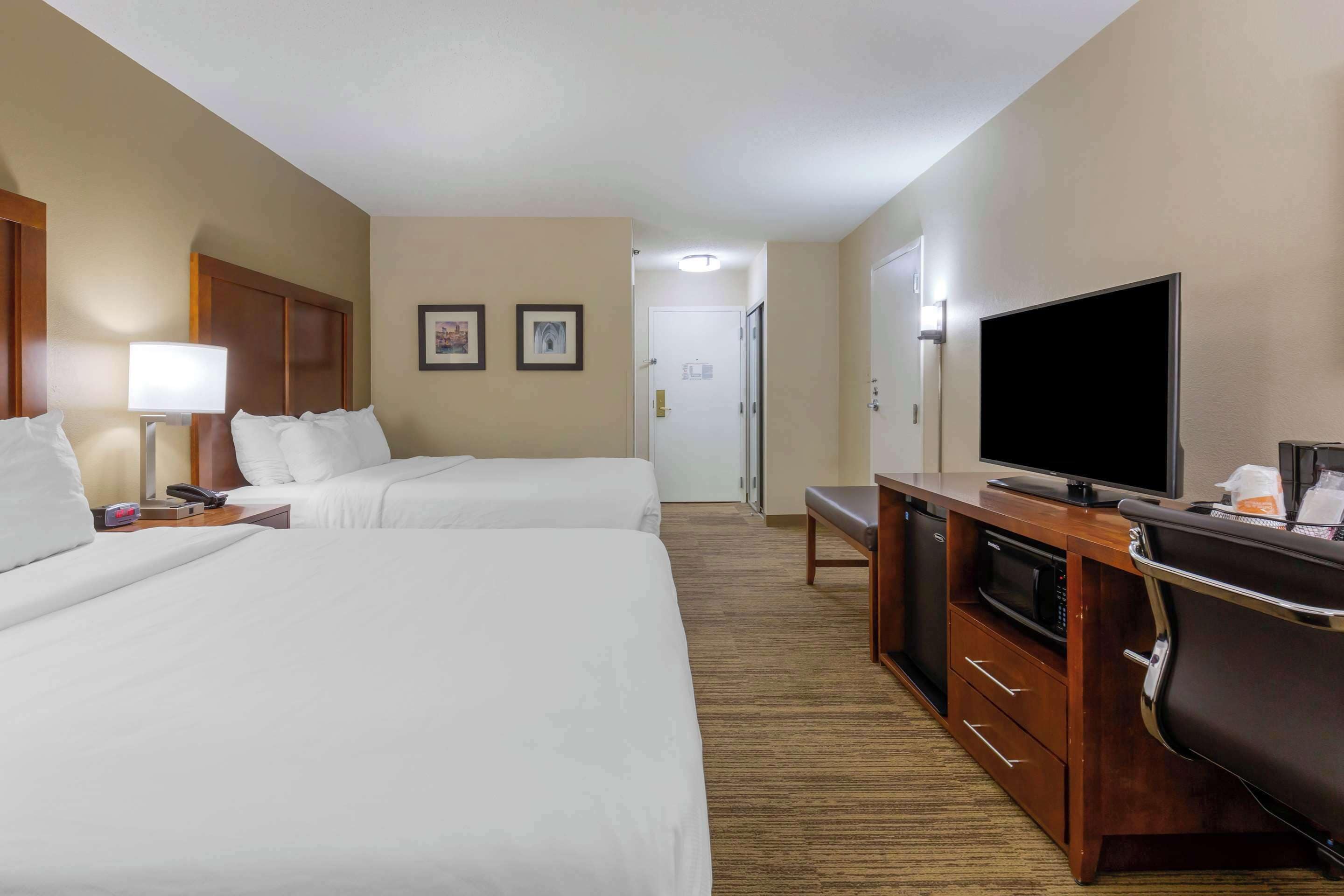 A hotel room with two beds, a TV, a desk with a microwave, and a door leading to a bathroom.