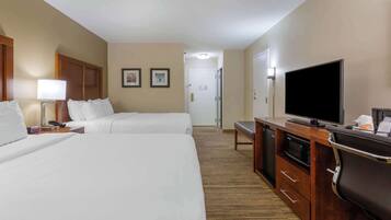 A hotel room with two beds, a TV, a desk with a microwave, and a door leading to a bathroom.