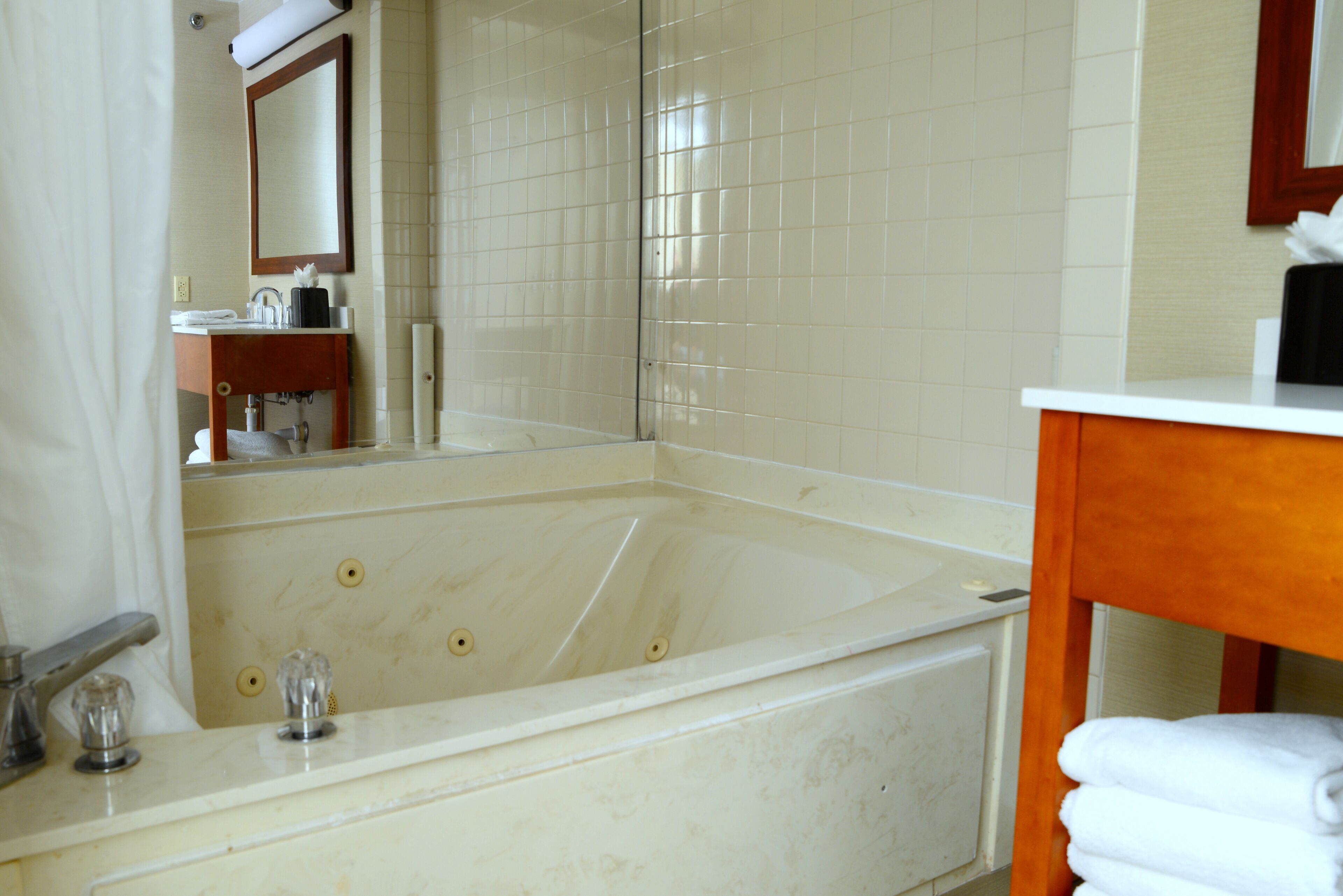 A bathroom with a large bathtub, a wooden vanity, and a mirror above the sink.