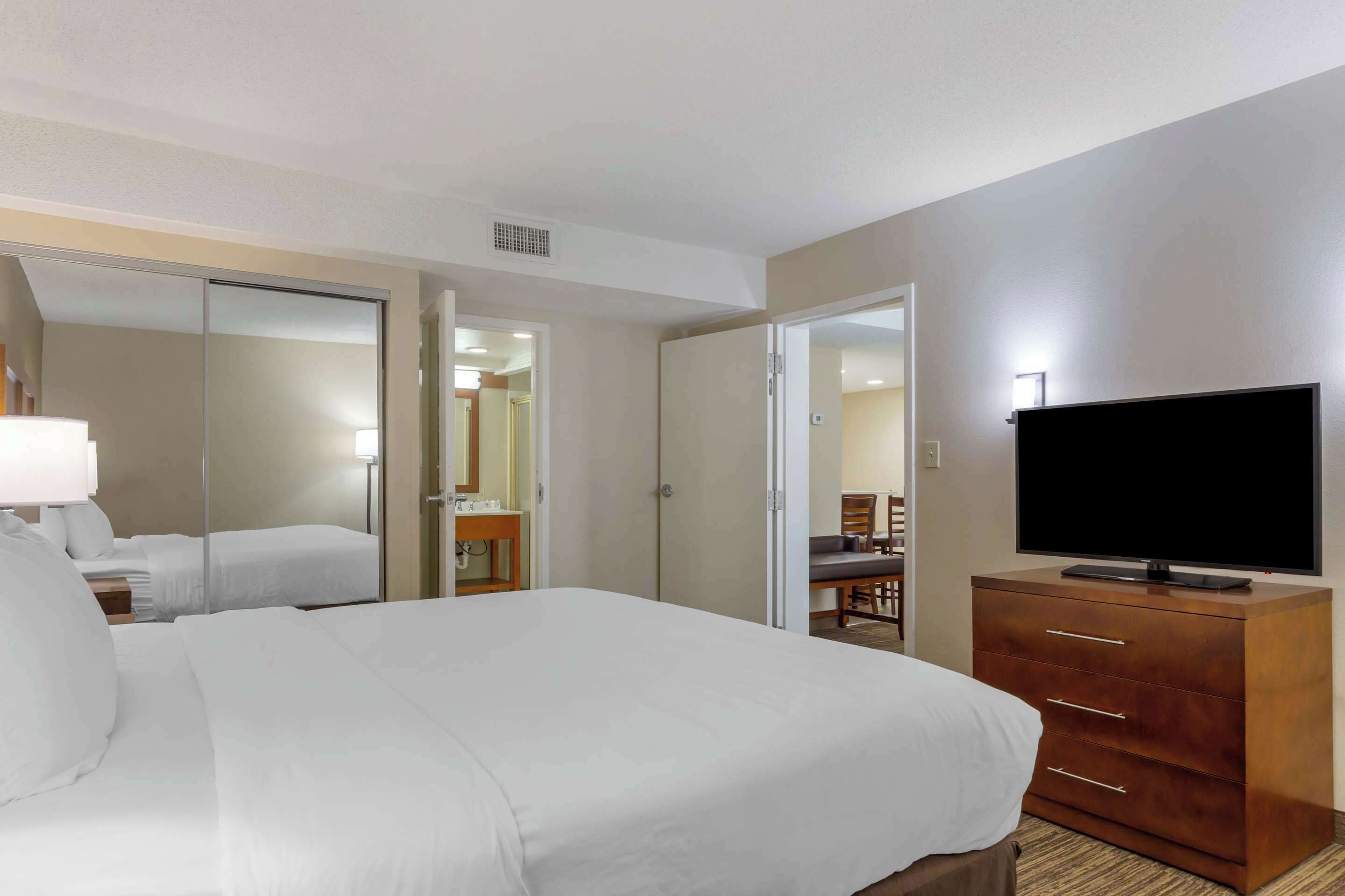 A hotel room with a large bed, a TV on a wooden dresser, and a mirror on the wall.