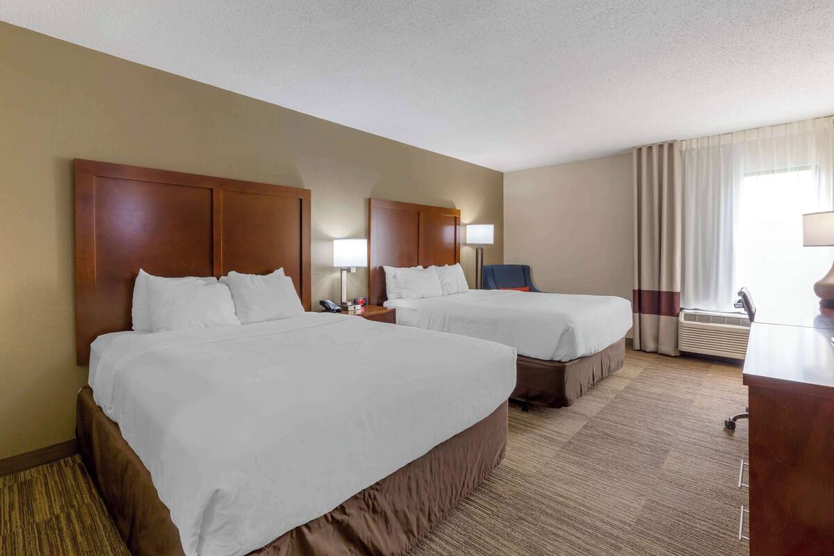Habitación de hotel con dos camas, un escritorio, una silla, una lámpara y una ventana con cortinas.