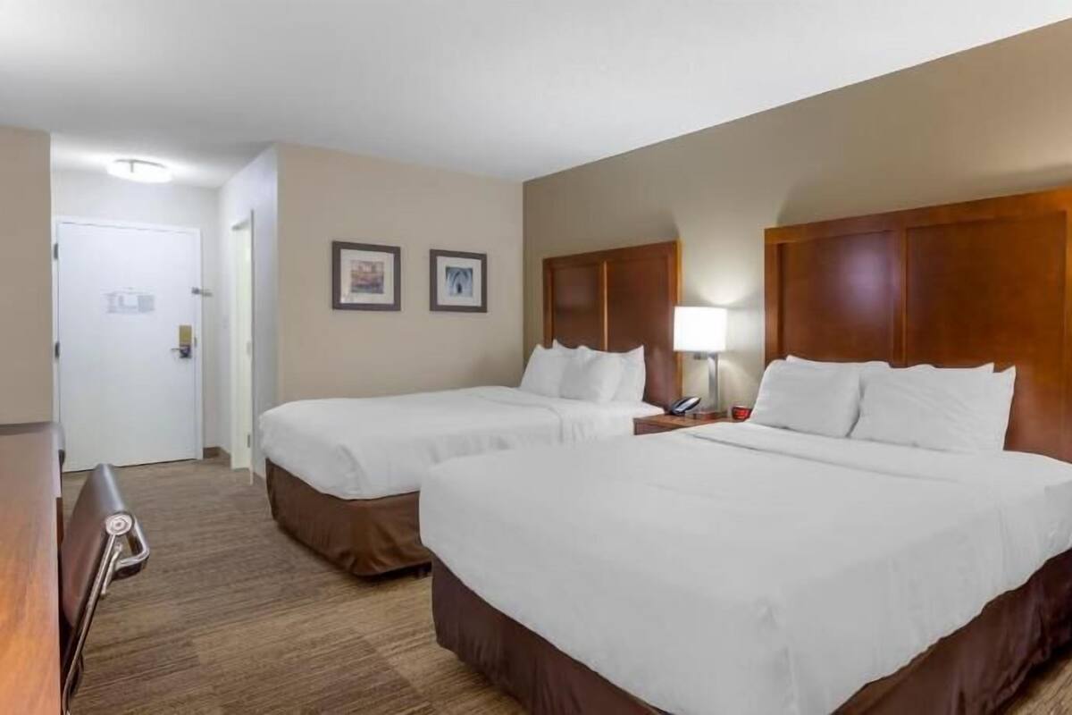 Habitación de hotel con dos camas, un escritorio, una silla y una lámpara.