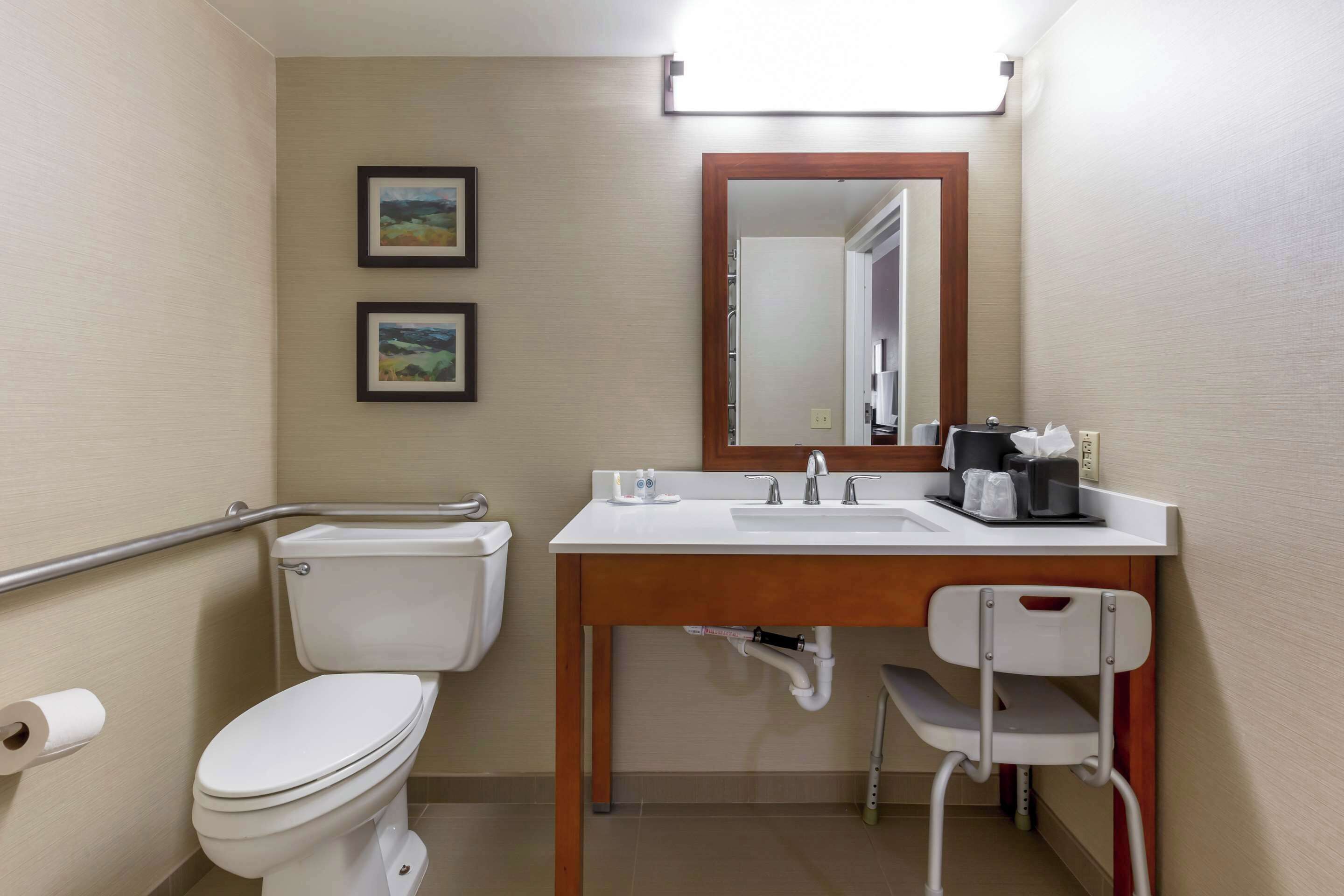 A bathroom with a toilet, a sink, a mirror, and a chair.