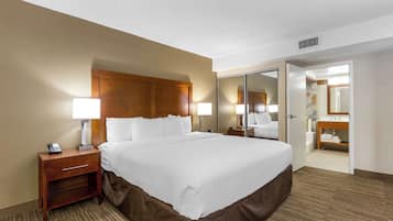 A hotel room with a large bed, bedside lamps, a nightstand, a mirror, and a bathroom visible through an open door.