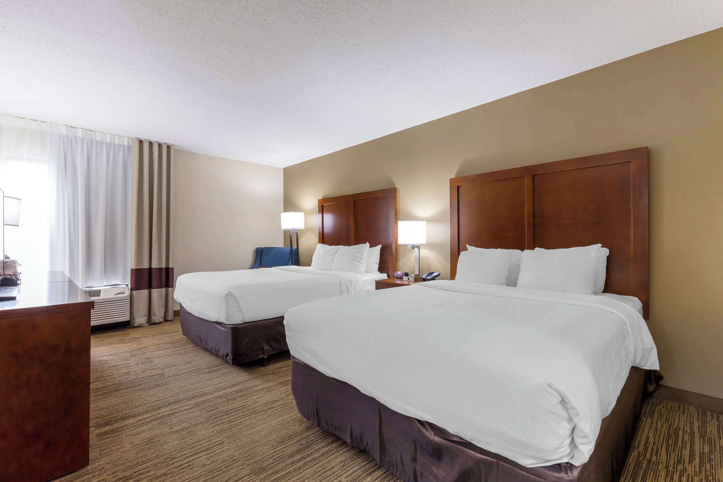 A hotel room with two beds, a desk, a chair, and a lamp.