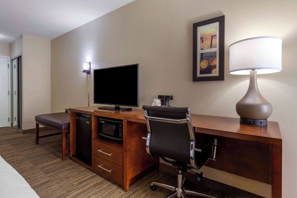 Habitación de hotel con escritorio de madera, televisor, lámpara, silla y cama.