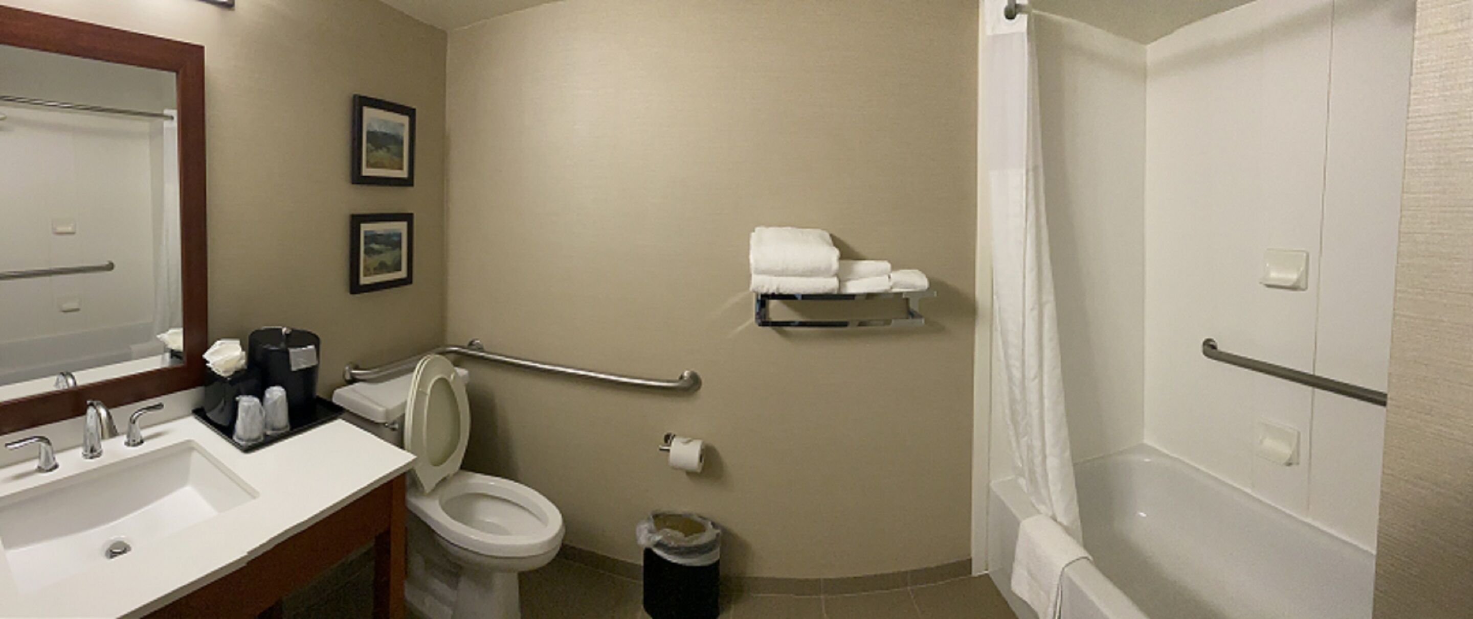Baño con lavamanos, inodoro y ducha. Hay toallas en un estante y un cubo de basura.