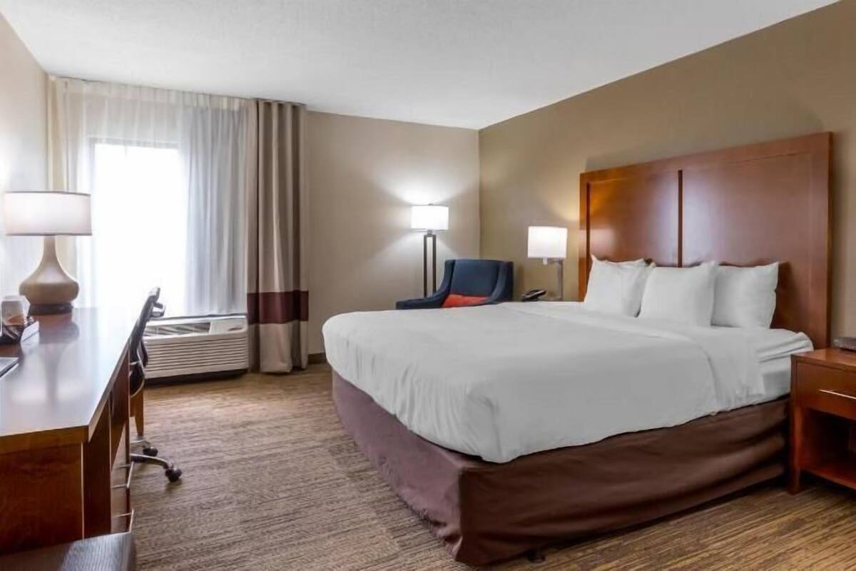 Una habitación de hotel con una cama grande, mesitas de noche, un escritorio y una silla.