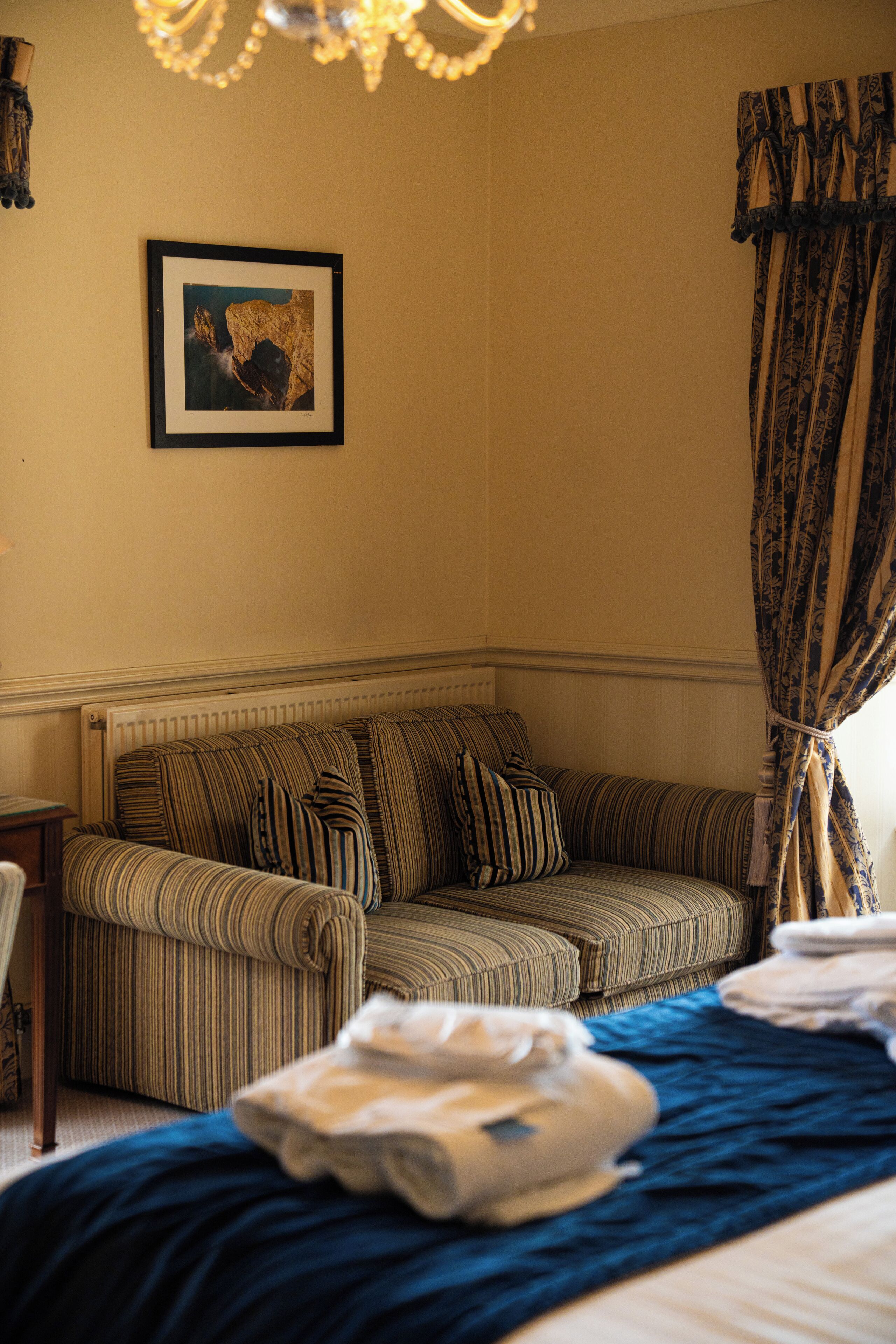 A hotel room with a striped sofa, a framed picture on the wall, and a bed with a blue blanket.