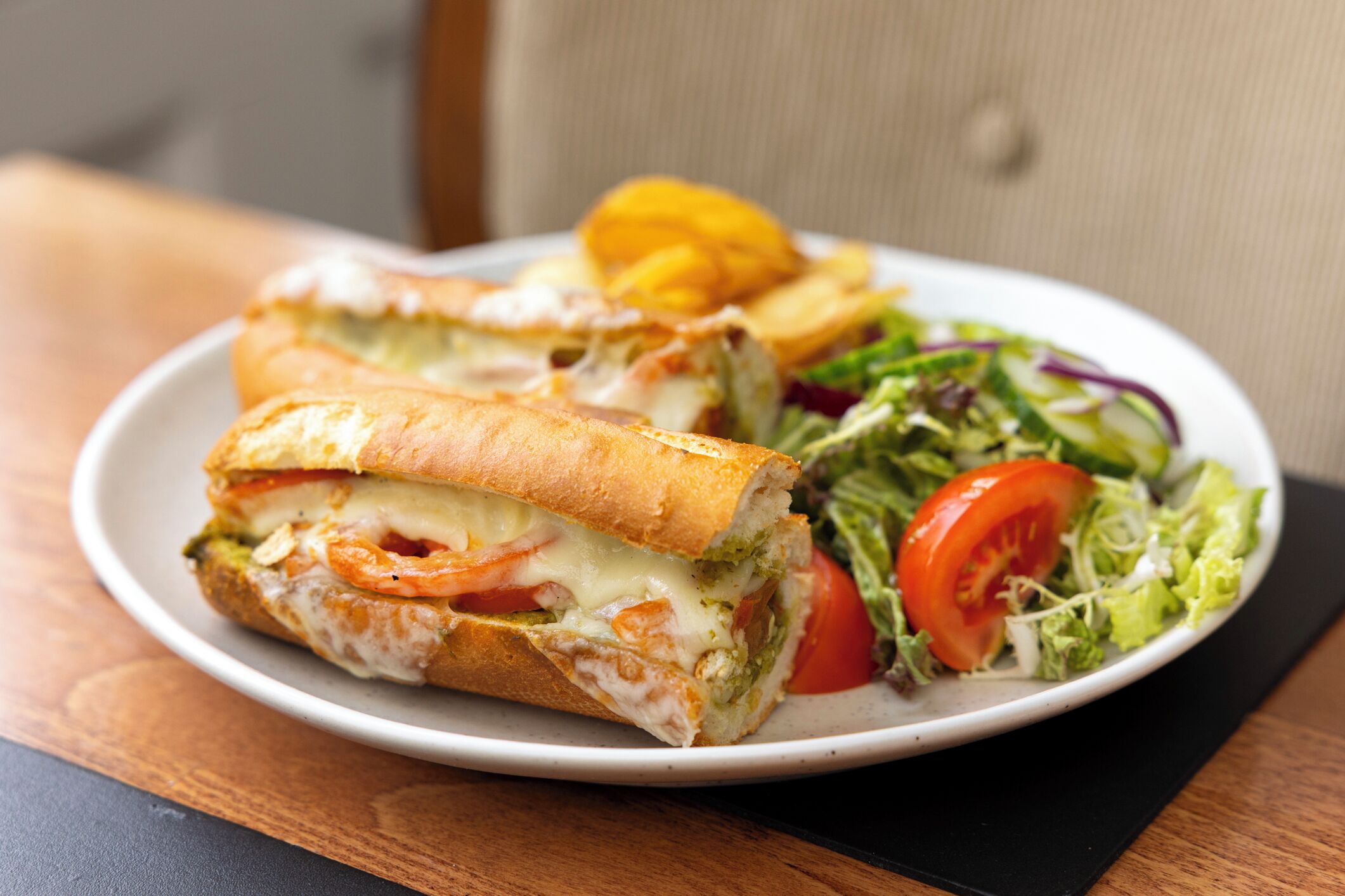 Un sándwich con lechuga, tomate y queso sobre un plato, acompañado de una ensalada y papas fritas.