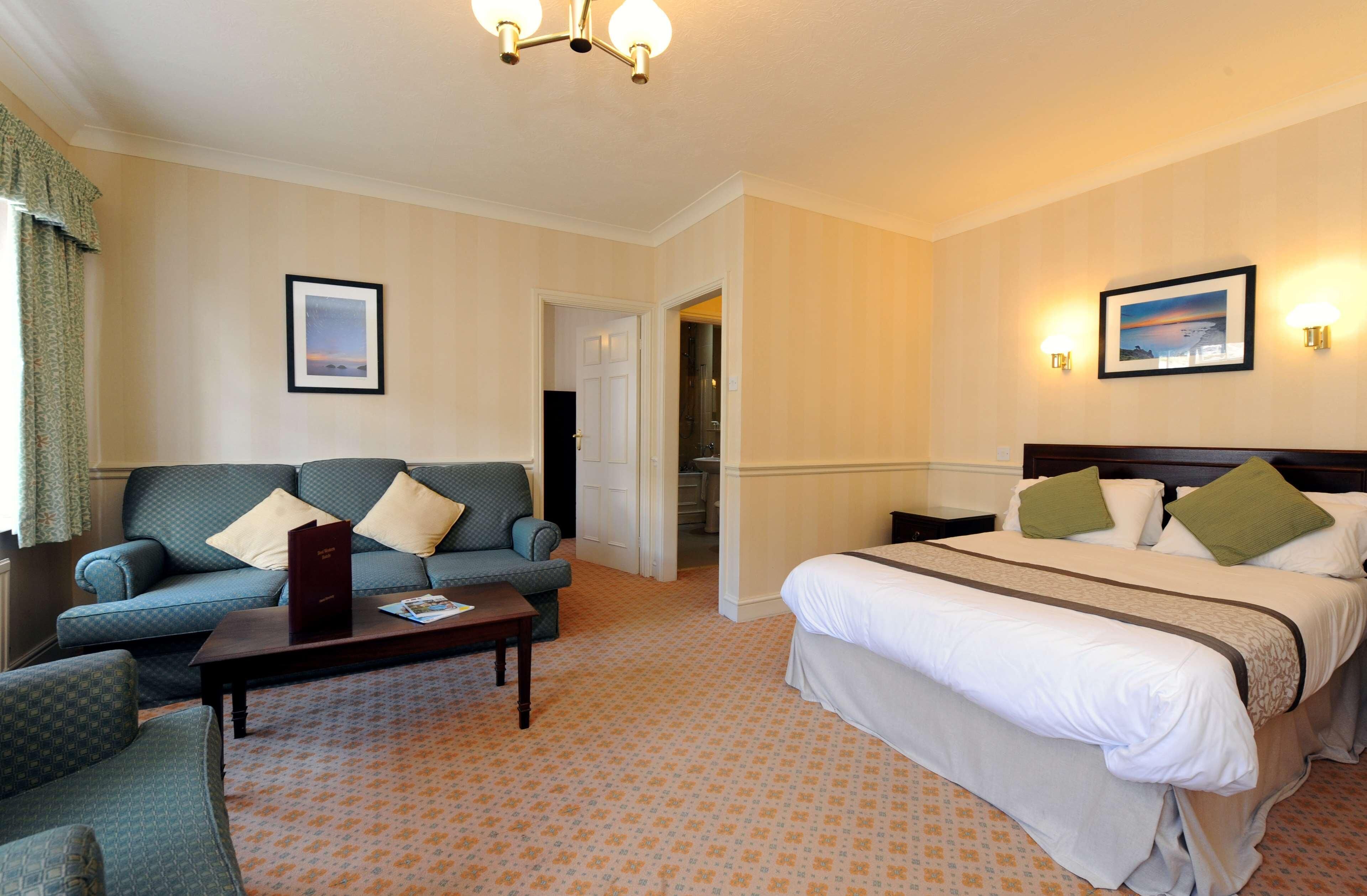 Una habitación de hotel con cama, sofá, mesita de centro y puerta que da a un baño.