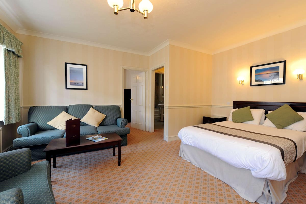 Una habitación de hotel con cama, sofá, mesita de centro y puerta que da a un baño.