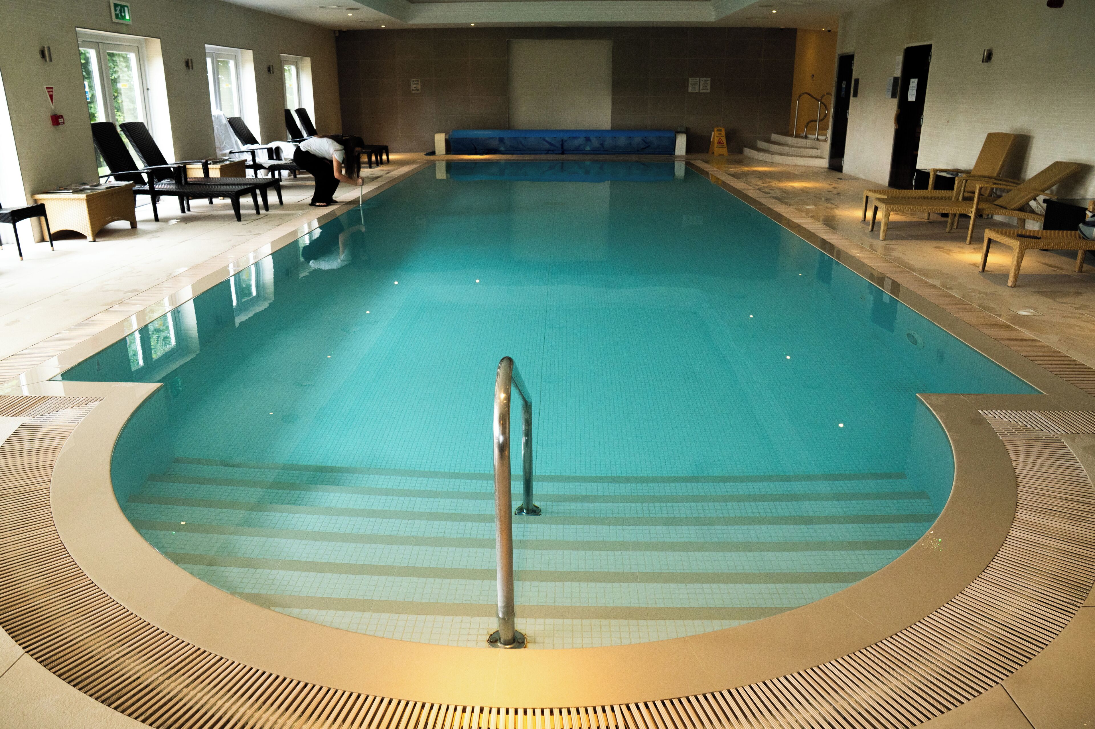 An indoor swimming pool with lounge chairs and a blue bench.