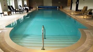An indoor swimming pool with lounge chairs and a blue bench.