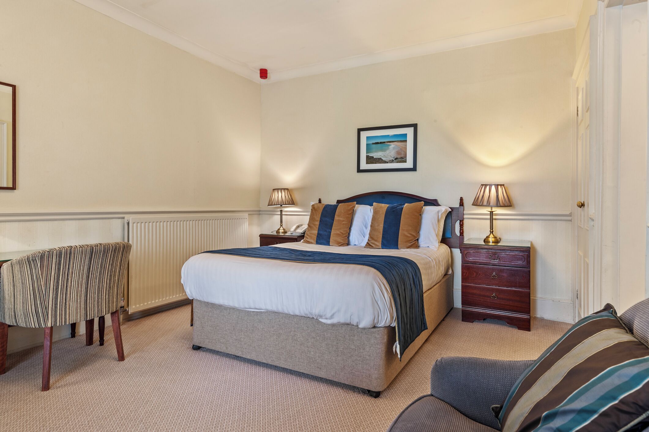 A neatly arranged bedroom with a large bed, bedside tables, a chair, and a radiator.