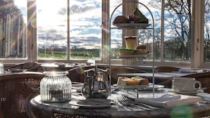 A sunlit dining area with a tiered dessert stand, wicker furniture, and a view of the outdoors. - Best Western Lamphey Court Hotel & Spa (Pembroke)