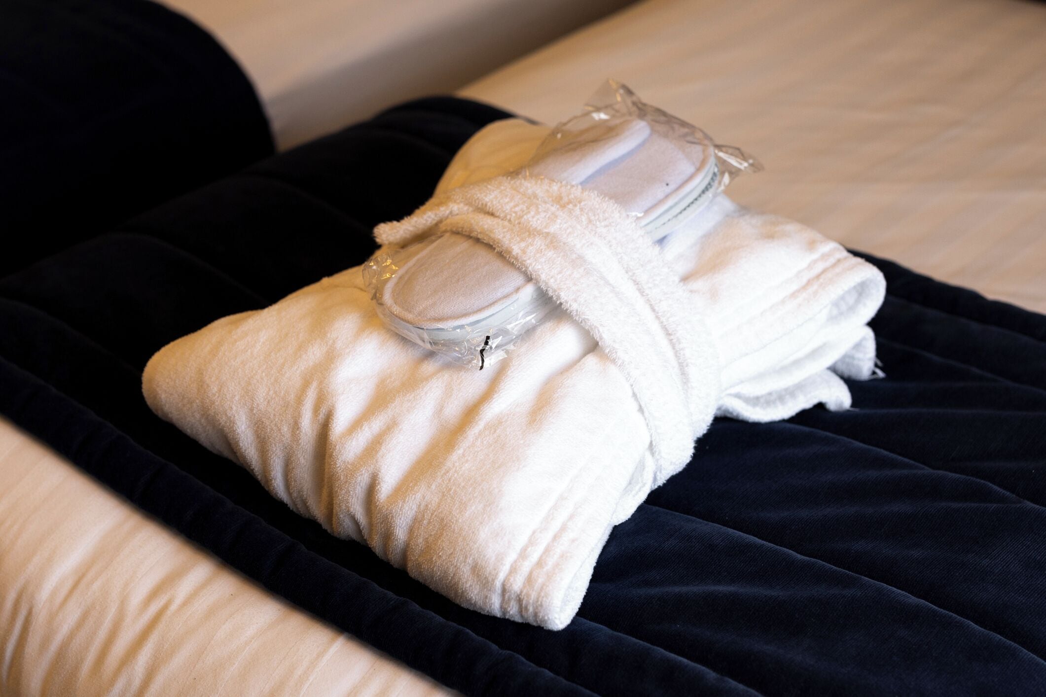 Et pænt foldet håndklæde og slippers på en mørkeblå dyne.