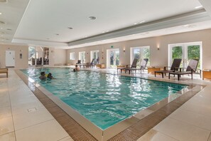A large indoor swimming pool with clear water, surrounded by lounge chairs and a tiled floor.