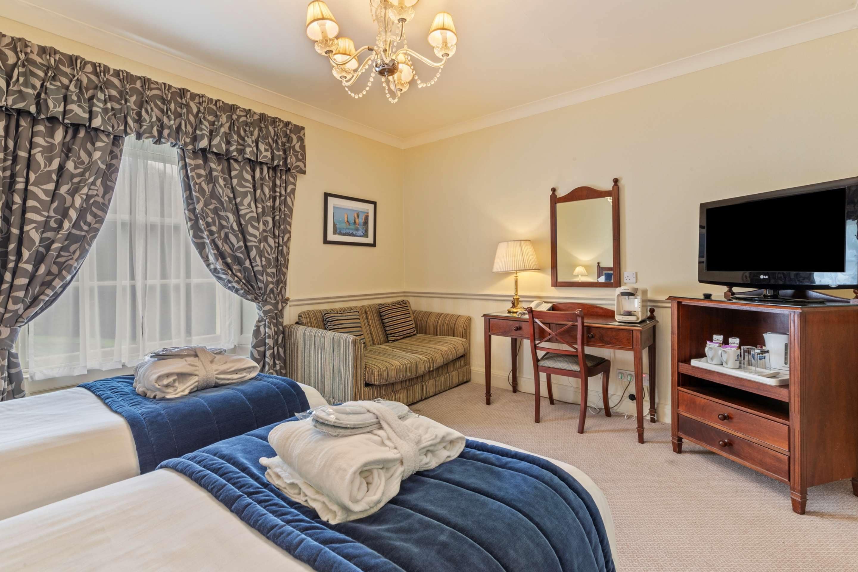 A hotel room with two beds, a desk with a chair, a television, and a dresser.