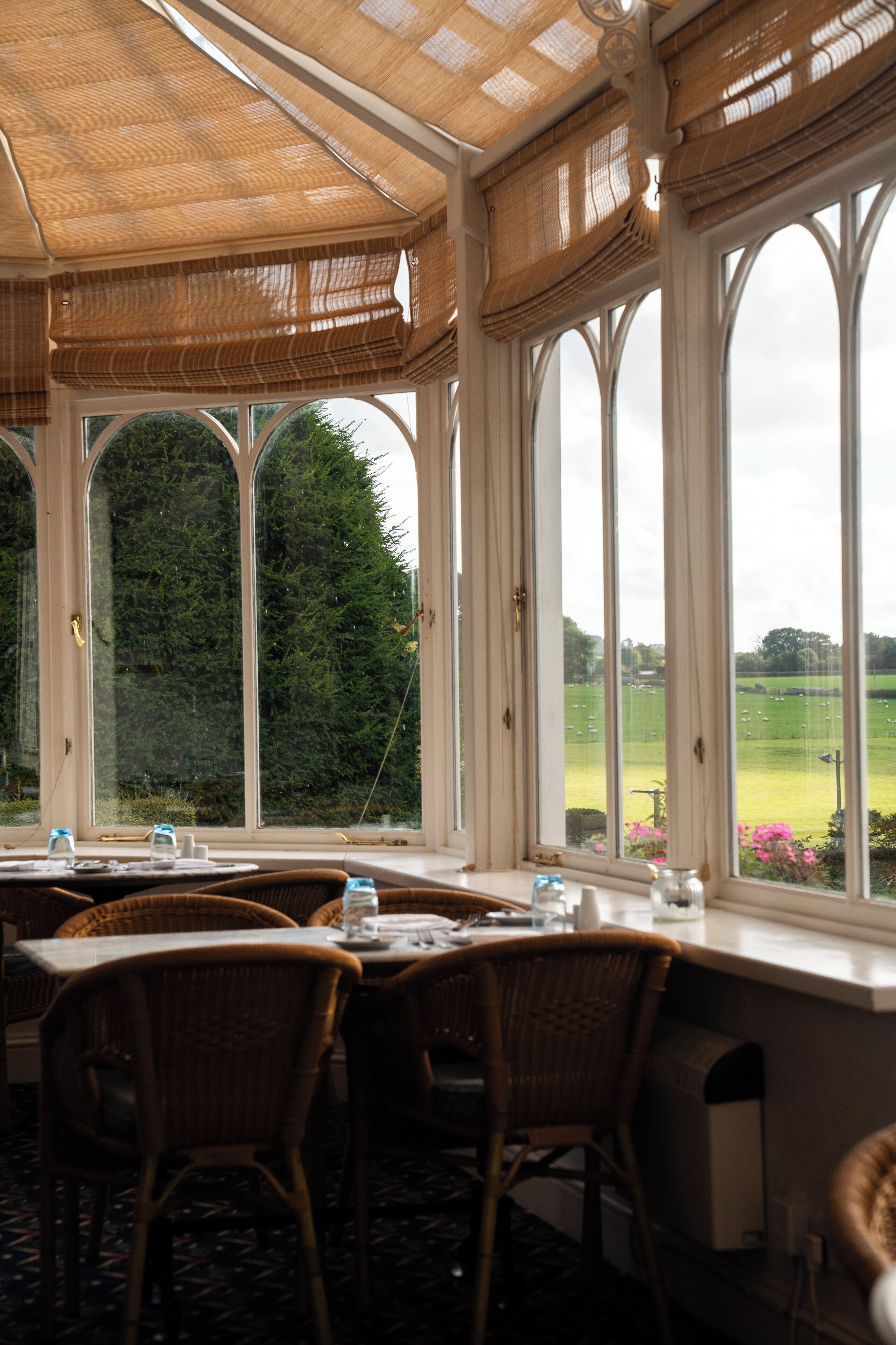 A conservatory with a table set for dining, large windows, and a view of a green landscape.