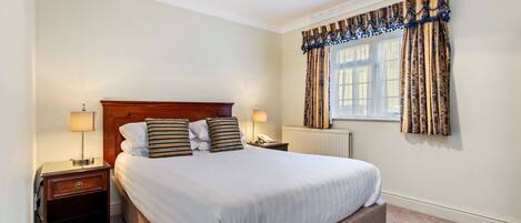 A neatly made bed with a wooden headboard, two bedside tables with lamps, and a window with patterned curtains.