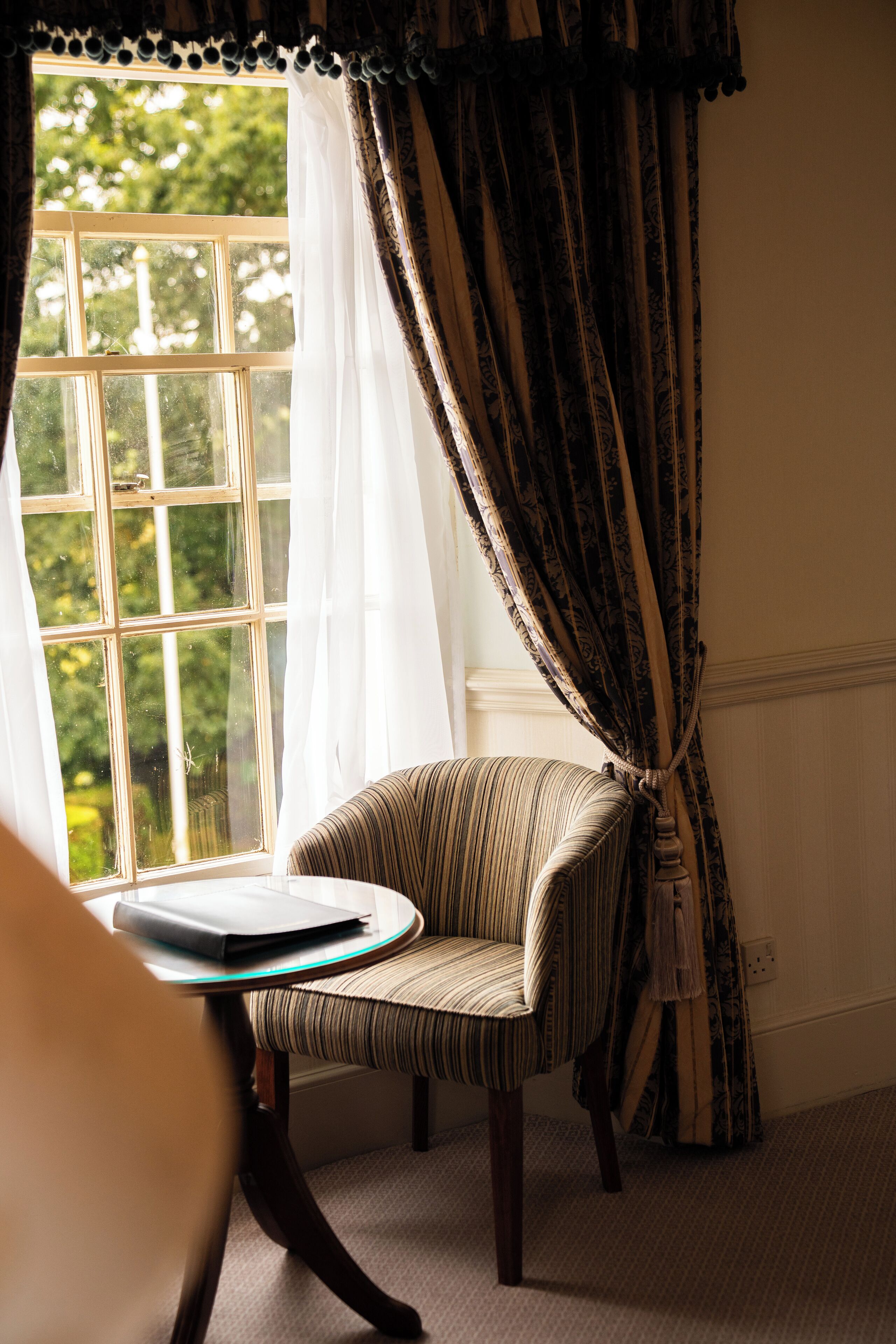 A room with a window, a chair, and a table with a book.