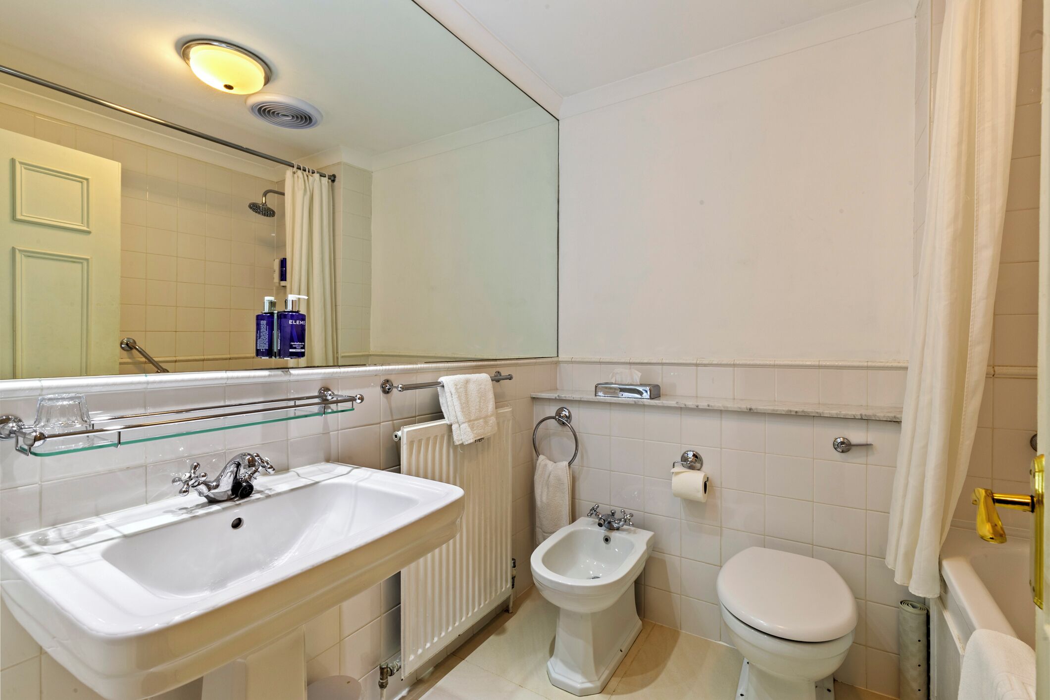 A bathroom with a sink, bidet, toilet, and a glass shelf.