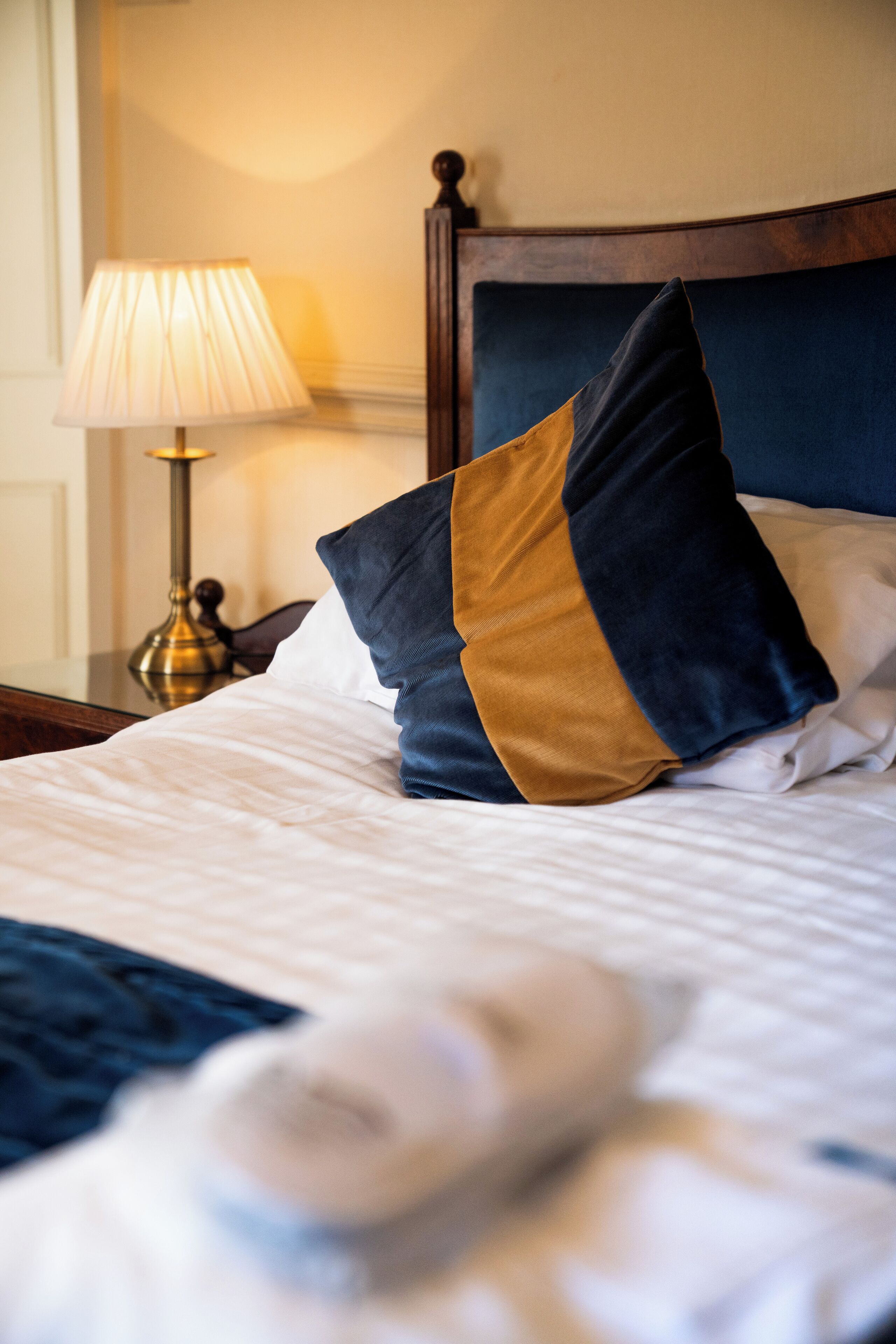 A neatly made bed with a blue and gold pillow, a white pillow, and a white blanket.