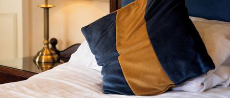 A neatly made bed with a blue and gold pillow, a white pillow, and a white blanket.