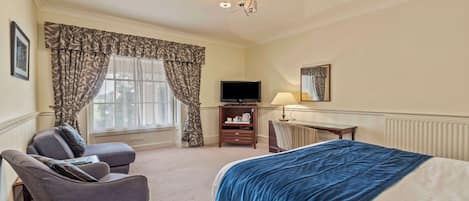 A hotel room with a bed, a sofa, a TV, a lamp, and a window with curtains.