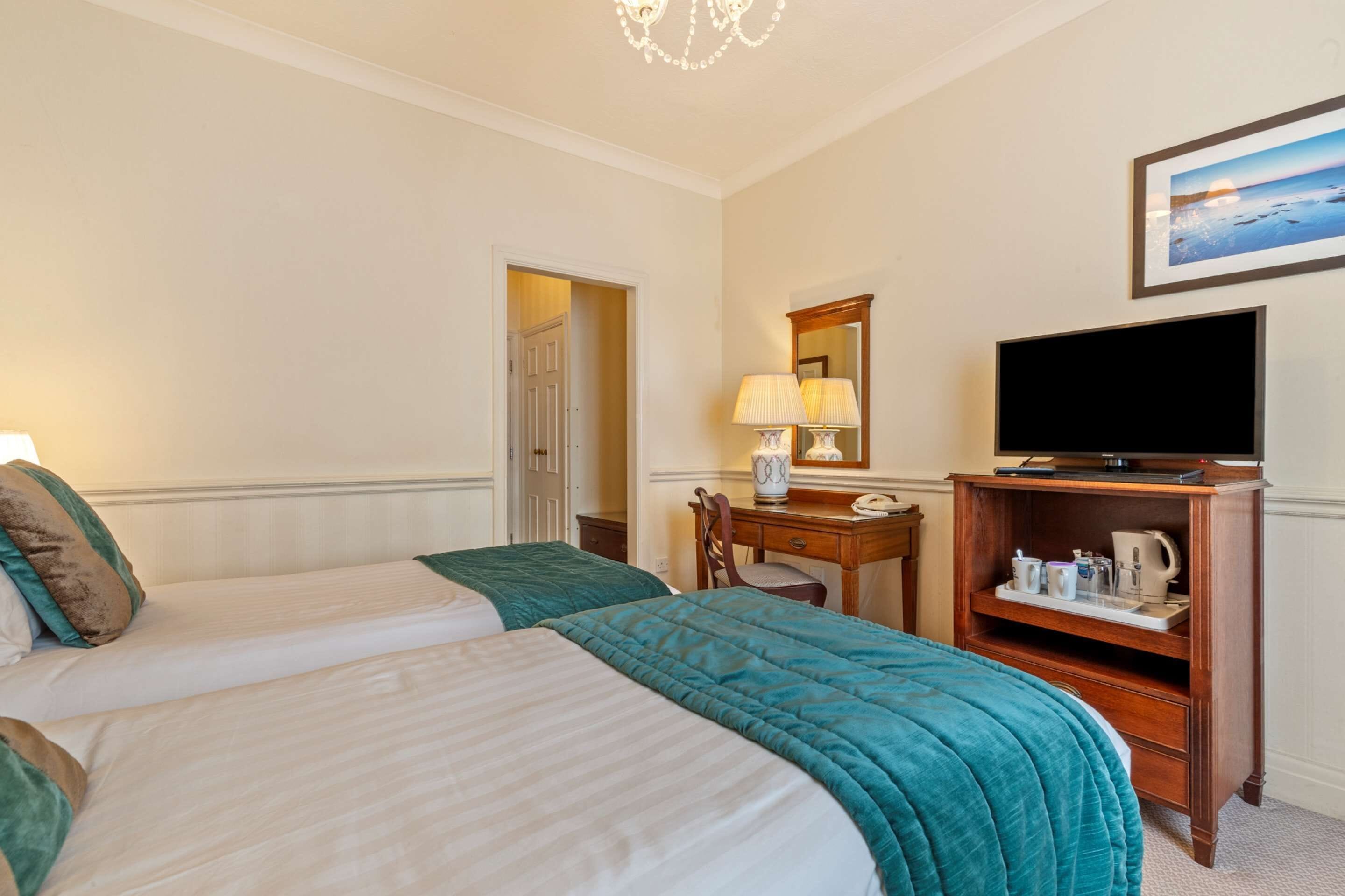 A hotel room with two beds, a television, a desk with a lamp, and a shelf with toiletries.