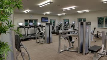 Une salle de sport équipée de tapis de course, d’appareils de musculation et d’un écran numérique.