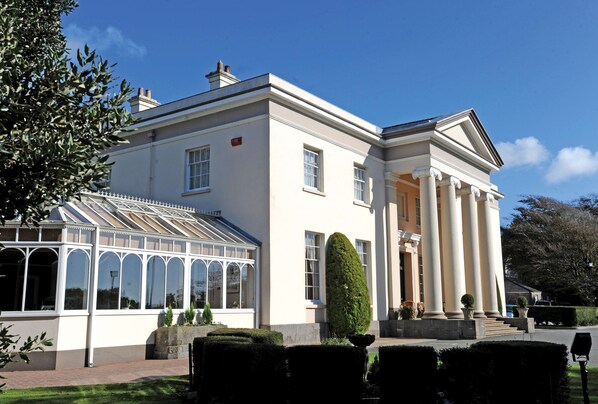 A large, white building with a conservatory and a symmetrical facade.