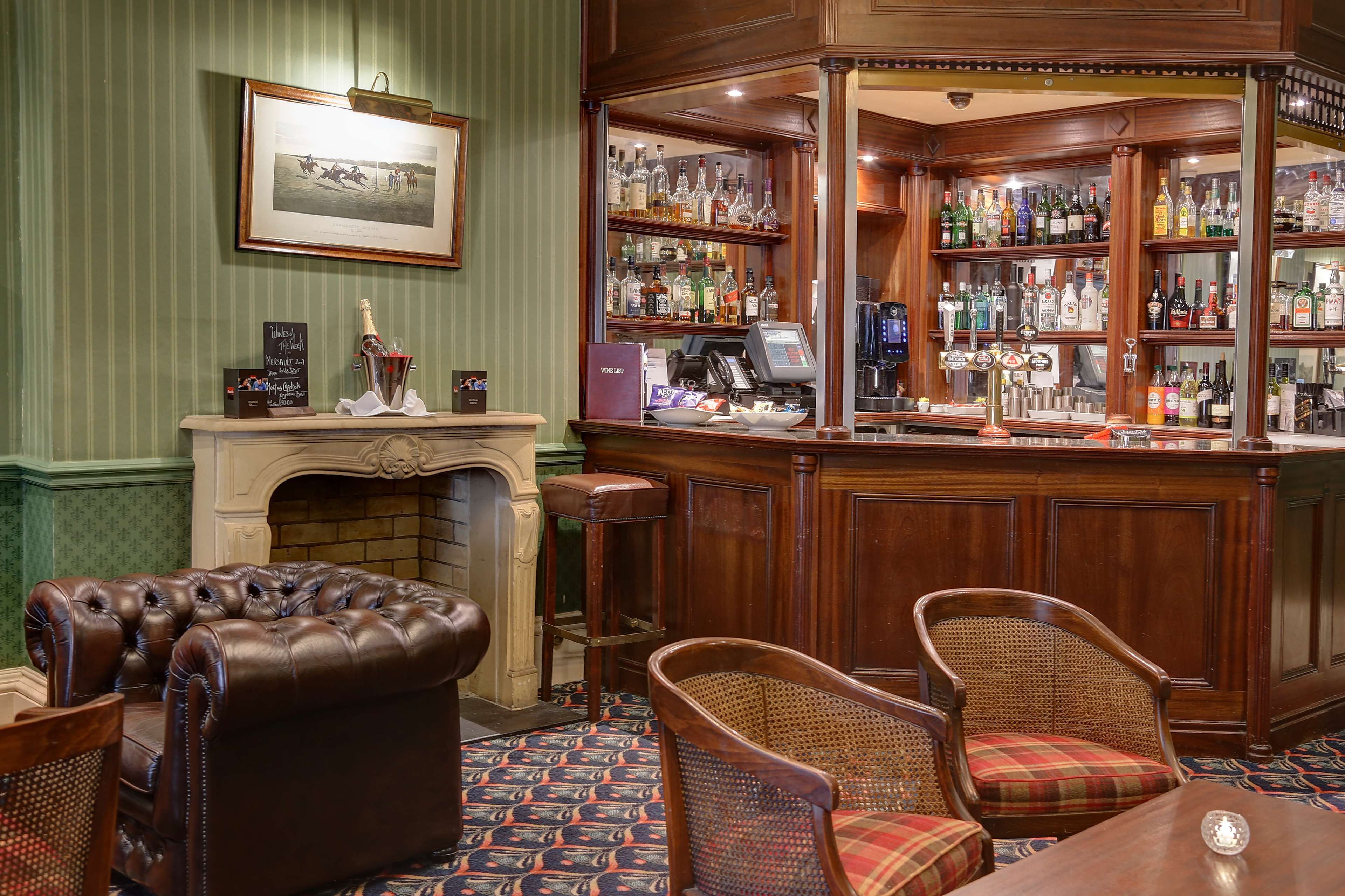 A bar area with a fireplace, leather armchair, wicker chairs, and a variety of liquor bottles.