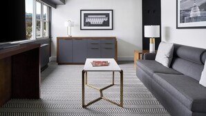 A modern hotel room with a large window, a flat-screen TV, a grey sofa, a small table, and a framed picture of a building on the wall. - ARC Hotel, Washington DC, Series by Marriott (Washington)