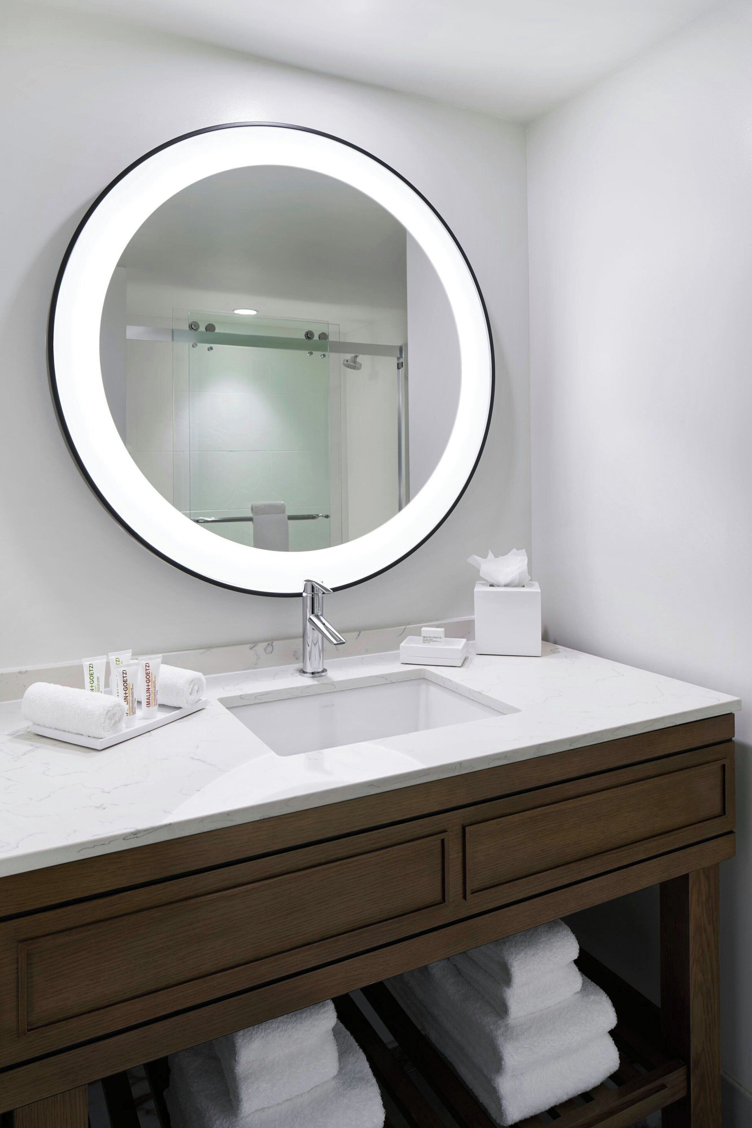 A bathroom with a round mirror, white sink, and wooden vanity.