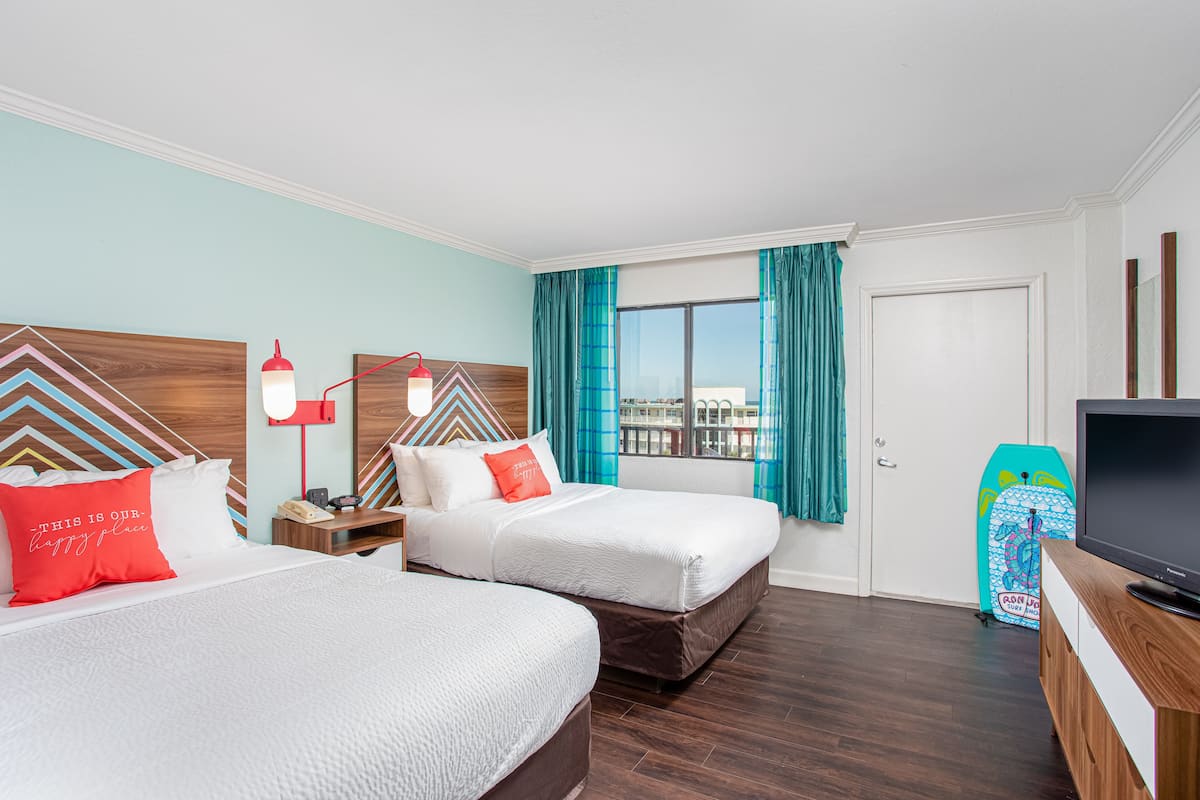 A hotel room with two beds, a TV, a nightstand, a lamp, and a window with curtains.