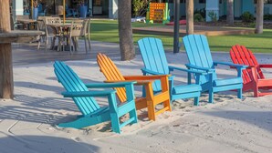 Outdoor seating with chairs and tables, a thatched roof structure, and a building with a sign in the background. - Beachside Hotel & Suites Cocoa Beach - Port Canaveral (Cocoa Beach)