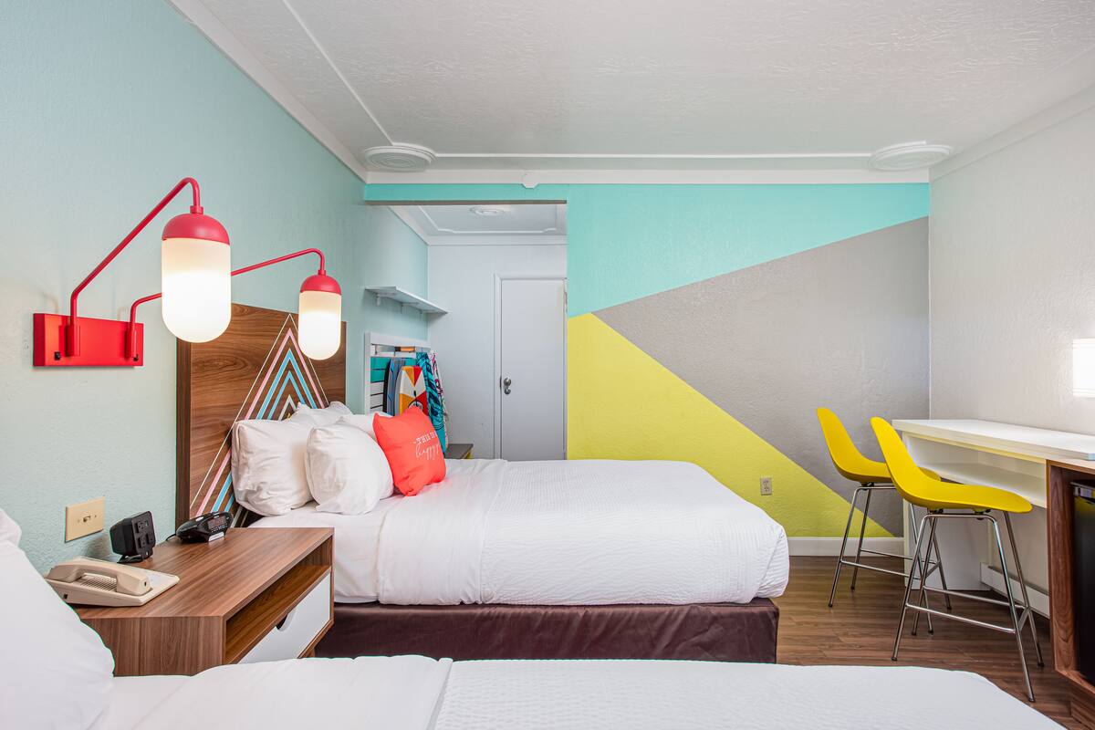 A hotel room with a bed, bedside table, lamp, two yellow chairs, and a desk.