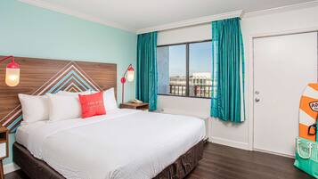 Una habitación de hotel con una cama grande, cabecera de madera, cortinas color turquesa, ventanal con vistas y una tabla de surf en la pared.