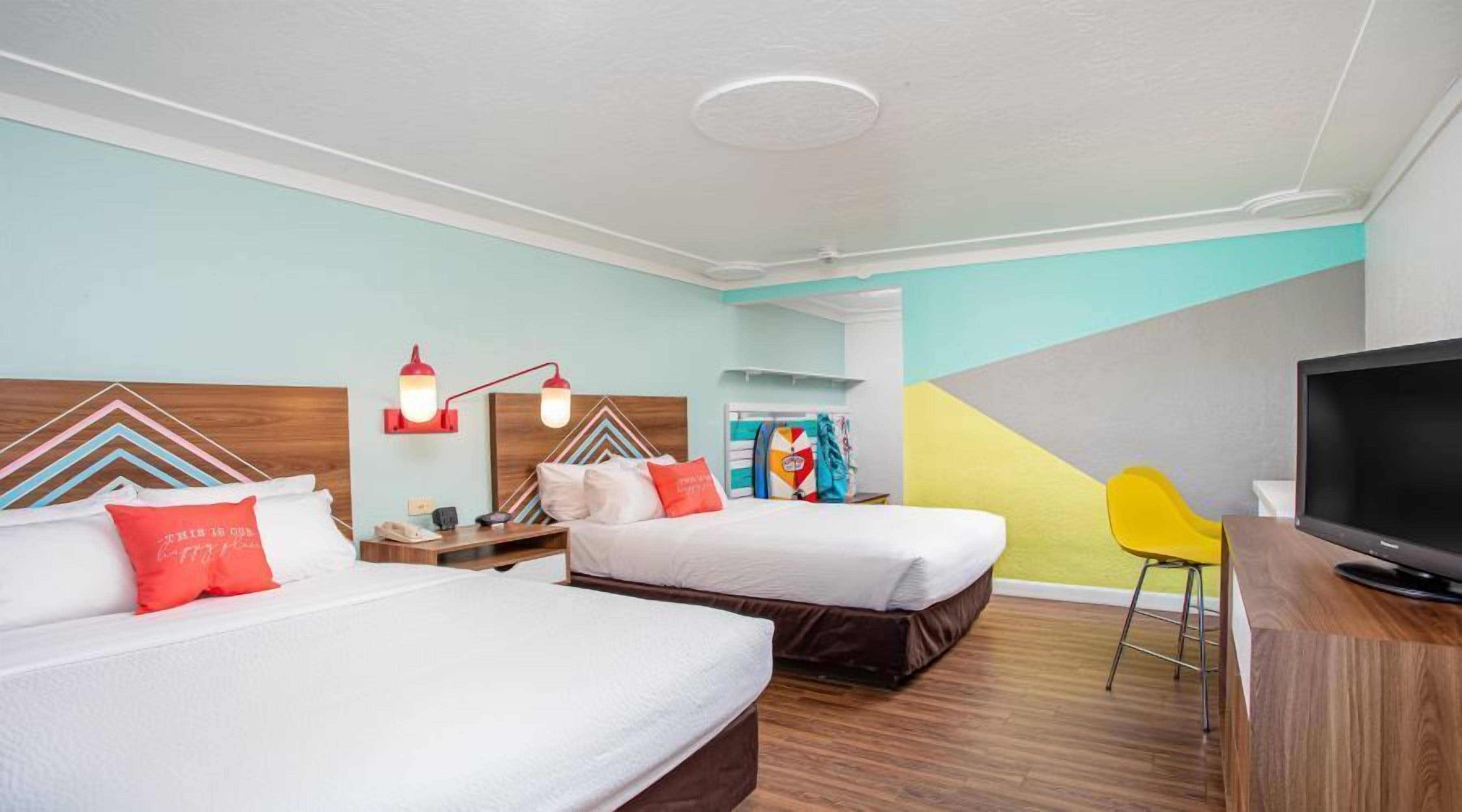 Habitación de hotel con dos camas, un escritorio con televisor y una silla.