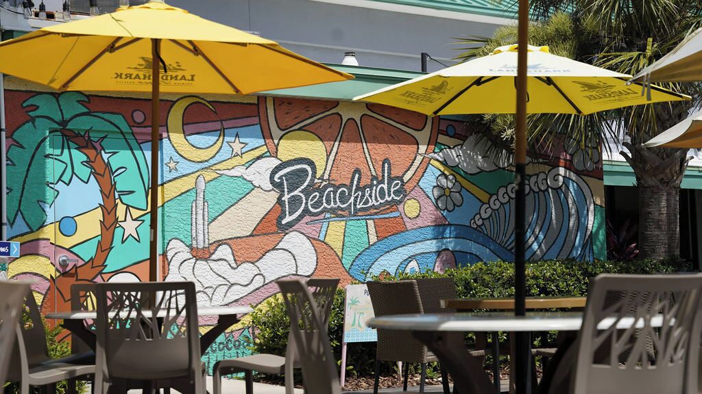 An outdoor seating area with tables and chairs under yellow umbrellas, featuring a colorful mural with the word "Beachside" prominently displayed.