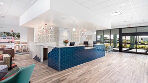 A modern reception area with a blue and white color scheme, a reception desk, seating area, and large windows offering views of the outdoors. - Beachside Hotel & Suites Cocoa Beach - Port Canaveral (Cocoa Beach)
