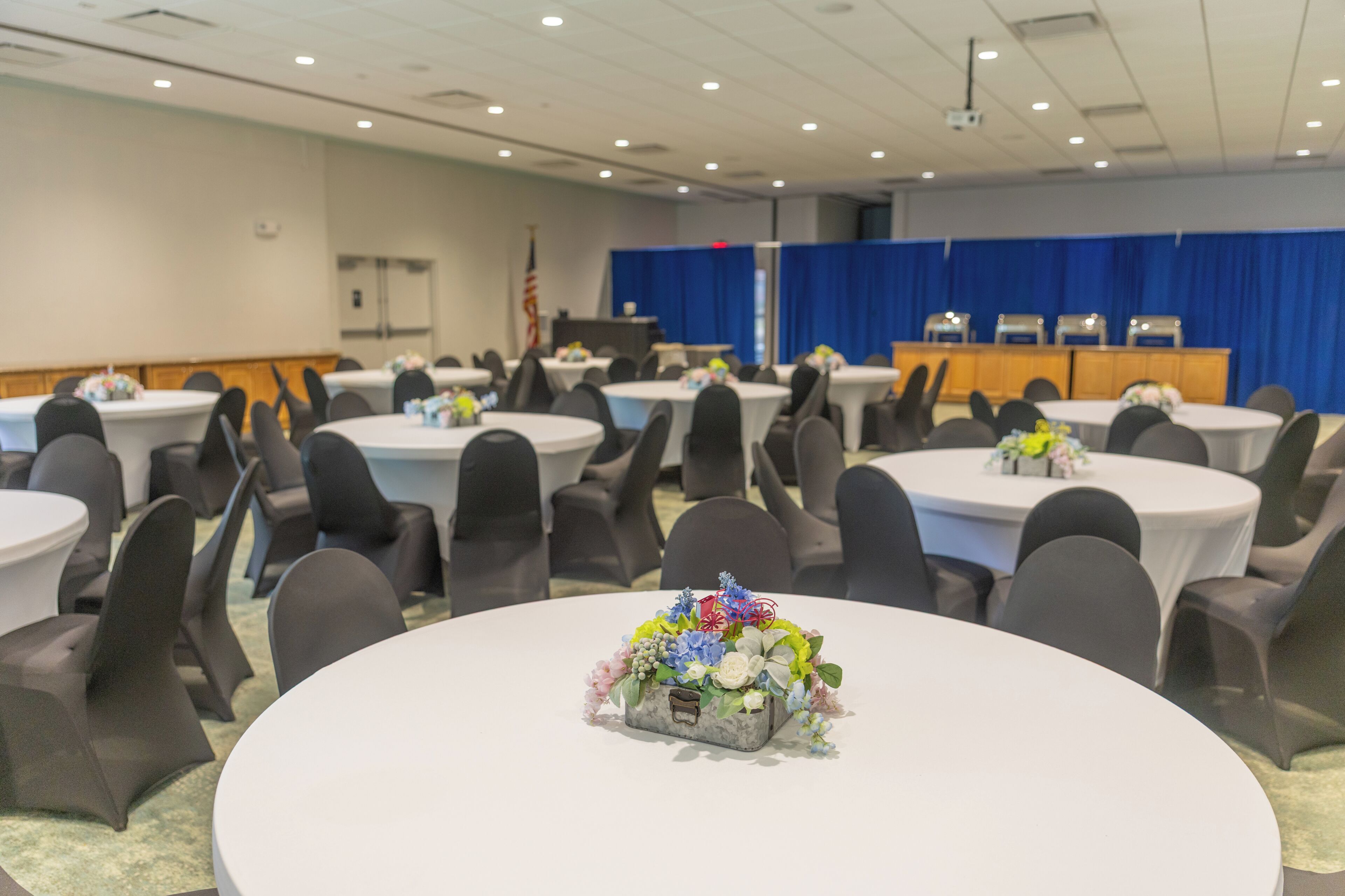 Un salón de conferencias con mesas redondas, sillas y un atril.